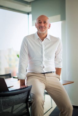 Modern bir ofiste ofis masasında yönetici bir işadamı duruyor. Orta yaşlı, profesyonel bir adam. Gömlek giyiyor ve kameraya gülümsüyor..