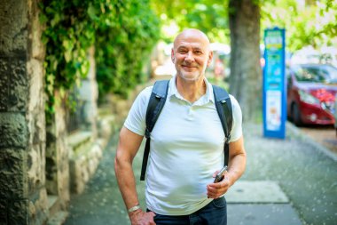 Şehirde sokakta yürüyen orta yaşlı bir adam. Gündelik giysiler ve sırt çantası giyen kendinden emin bir erkek..