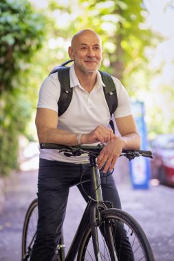 Şehirde bisikletli bir banliyö. Son sınıf öğrencisi sokakta bisiklet sürüyor. Gündelik giysiler ve sırt çantası giyen kendinden emin bir erkek.. 