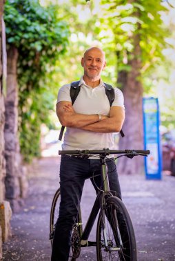 Şehirde bisikletli bir banliyö. Son sınıf öğrencisi sokakta bisiklet sürüyor. Gündelik giysiler ve sırt çantası giyen kendinden emin bir erkek.. 