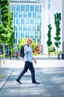 Yakışıklı bir adam dizüstü bilgisayar tutuyor ve şehirde finans sektöründe yürüyor. Orta yaşlı işadamı iş kıyafeti giyiyor ve telefon görüşmesi yapıyor.. 