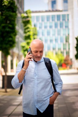 Yakışıklı bir adam dizüstü bilgisayar tutuyor ve şehirde finans sektöründe yürüyor. Orta yaşlı işadamı iş kıyafeti giyiyor ve telefon görüşmesi yapıyor.. 