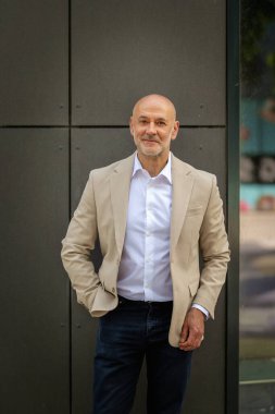 Gri bir duvarın önünde caddede duran orta yaşlı bir adam. İş kıyafeti giymiş yakışıklı bir iş adamı.. 