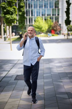 Yakışıklı bir adam dizüstü bilgisayar tutuyor ve şehirde finans sektöründe yürüyor. Orta yaşlı işadamı iş kıyafeti giyiyor ve telefon görüşmesi yapıyor.. 
