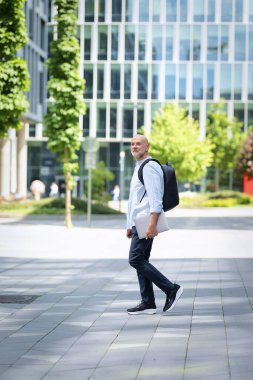 Yakışıklı bir adam dizüstü bilgisayar tutuyor ve şehirde finans sektöründe yürüyor. Sıradan kıyafetler giyen orta yaşlı bir iş adamı. Tam boy çekim. 