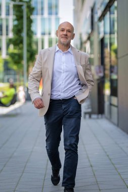 Şehirde finans sektöründe yürüyen yakışıklı bir adam. Orta yaşlı iş adamı günlük iş kıyafetleri giyiyor. Tam boy çekim. 