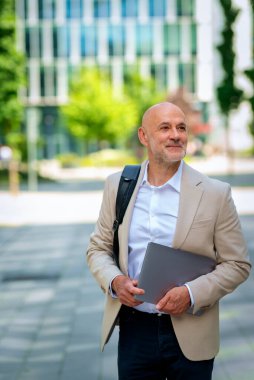 Yakışıklı bir adam dizüstü bilgisayar tutuyor ve şehirde finans sektöründe yürüyor. Orta yaşlı işadamı iş kıyafeti giyiyor.. 