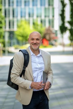 Yakışıklı bir adam dizüstü bilgisayar tutuyor ve şehirde finans sektöründe yürüyor. Orta yaşlı işadamı iş kıyafeti giyiyor.. 