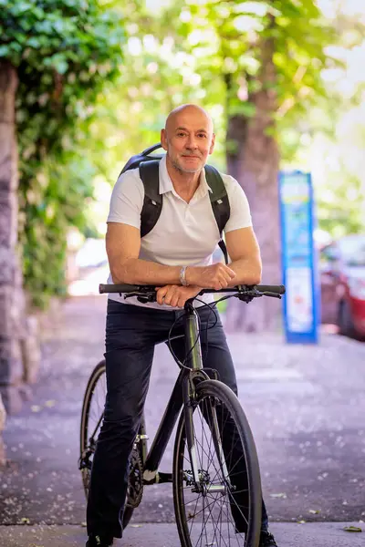 Şehirde bisikletli bir banliyö. Son sınıf öğrencisi sokakta bisiklet sürüyor. Gündelik giysiler ve sırt çantası giyen kendinden emin bir erkek.. 