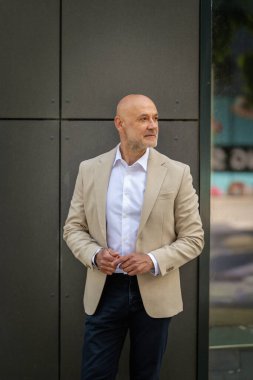 Gri bir duvarın önünde caddede duran orta yaşlı bir adam. İş kıyafeti giymiş yakışıklı bir iş adamı.. 