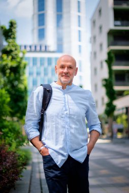 Şehir caddesinde yürüyen orta yaşlı bir adam. Tişört ve sırt çantası giyen kendinden emin bir erkek.. 