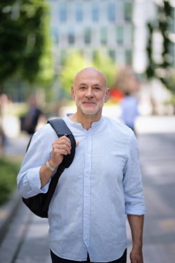Şehir caddesinde yürüyen orta yaşlı bir adam. Tişört ve sırt çantası giyen kendinden emin bir erkek.. 
