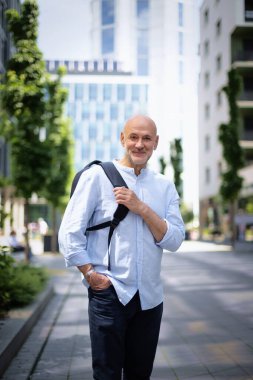 Şehir caddesinde yürüyen orta yaşlı bir adam. Tişört ve sırt çantası giyen kendinden emin bir erkek.. 