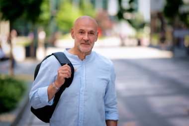 Şehir caddesinde yürüyen orta yaşlı bir adam. Tişört ve sırt çantası giyen kendinden emin bir erkek.. 