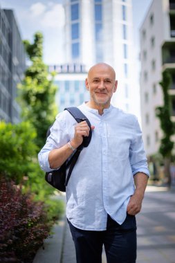 Şehir caddesinde yürüyen orta yaşlı bir adam. Tişört ve sırt çantası giyen kendinden emin bir erkek.. 