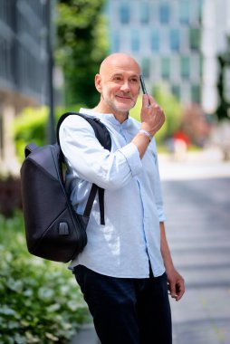 Yakışıklı bir adam dizüstü bilgisayar tutuyor ve şehirde finans sektöründe yürüyor. Orta yaşlı işadamı iş kıyafeti giyiyor ve telefon görüşmesi yapıyor.. 