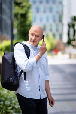Yakışıklı bir adam dizüstü bilgisayar tutuyor ve şehirde finans sektöründe yürüyor. Orta yaşlı işadamı iş kıyafeti giyiyor ve telefon görüşmesi yapıyor.. 
