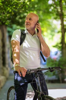 Şehirde bisikletli bir banliyö. Son sınıf öğrencisi sokakta bisiklet sürüyor ve akıllı telefonunu kullanıyor. Gündelik giysiler ve sırt çantası giyen kendinden emin bir erkek.. 