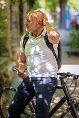 Şehirde bisikletli bir banliyö. Son sınıf öğrencisi sokakta bisiklet sürüyor ve akıllı telefonunu kullanıyor. Gündelik giysiler ve sırt çantası giyen kendinden emin bir erkek.. 