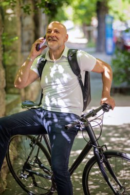 Şehirde bisikletli bir banliyö. Son sınıf öğrencisi sokakta bisiklet sürüyor ve akıllı telefonunu kullanıyor. Gündelik giysiler ve sırt çantası giyen kendinden emin bir erkek.. 