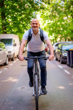 Sokakta bisiklet kullanan orta yaşlı bir adam. Banliyö çalışanı işe gidiyor ve günlük giysiler giyiyor. Tam uzunluk. 