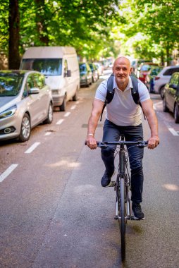 Sokakta bisiklet kullanan orta yaşlı bir adam. Banliyö çalışanı işe gidiyor ve günlük giysiler giyiyor. Tam uzunluk. 