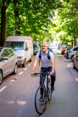 Sokakta bisiklet kullanan orta yaşlı bir adam. Banliyö çalışanı işe gidiyor ve günlük giysiler giyiyor. Tam uzunluk. 