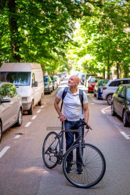 Sokakta bisiklet kullanan orta yaşlı bir adam. Banliyö çalışanı işe gidiyor ve günlük giysiler giyiyor. Tam uzunluk. 