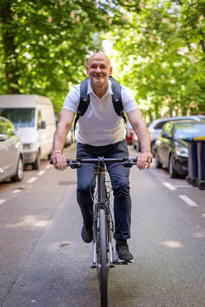 Sokakta bisiklet kullanan orta yaşlı bir adam. Banliyö çalışanı işe gidiyor ve günlük giysiler giyiyor. Tam uzunluk. 