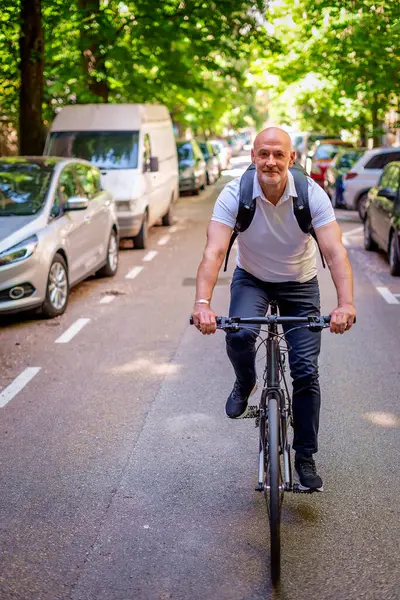 Sokakta bisiklet kullanan orta yaşlı bir adam. Banliyö çalışanı işe gidiyor ve günlük giysiler giyiyor. Tam uzunluk. 