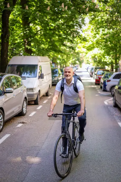 Sokakta bisiklet kullanan orta yaşlı bir adam. Banliyö çalışanı işe gidiyor ve günlük giysiler giyiyor. Tam uzunluk. 
