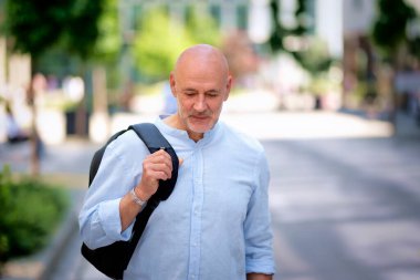 Şehir caddesinde yürüyen orta yaşlı bir adam. Tişört ve sırt çantası giyen kendinden emin bir erkek.. 