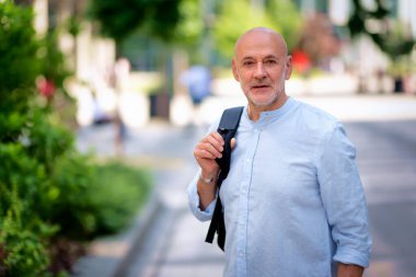 Şehir caddesinde yürüyen orta yaşlı bir adam. Tişört ve sırt çantası giyen kendinden emin bir erkek.. 