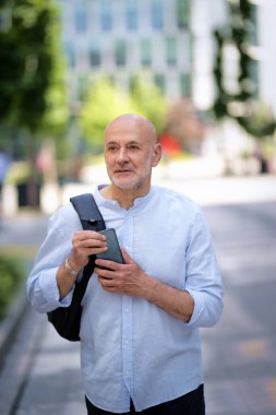 Şehir caddesinde yürüyen ve elinde akıllı bir telefon tutan orta yaşlı bir adam. Tişört ve sırt çantası giyen kendinden emin bir erkek.. 