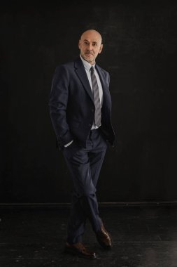 Tecrit edilmiş siyah arka plana karşı duran yaşlı bir adamın tam uzunluğu. Uzayı kopyala Orta yaşlı iş adamı takım elbise ve kravat takıyor.. 