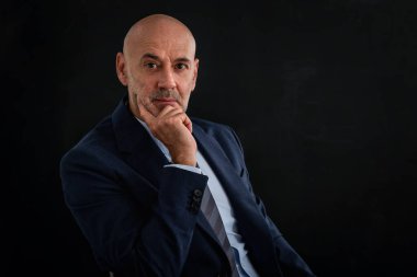 Orta yaşlı bir adamın izole edilmiş arka planda çekilmiş bir fotoğrafı. Kendine güvenen erkek takım elbiseli ve kameraya bakıyor. Uzayı kopyala Eller çenede.. 