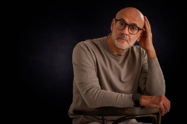 Siyah arka planda oturan balıkçı yaka kazaklı orta yaşlı bir adam. İzole edilmiş arka plan. Boşluğu kopyala.