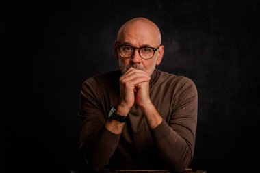 Siyah arka planda oturan balıkçı yaka kazaklı orta yaşlı bir adam. İzole edilmiş arka plan. Boşluğu kopyala.