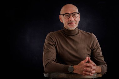 Siyah arka planda oturan balıkçı yaka kazaklı orta yaşlı bir adam. İzole edilmiş arka plan. Boşluğu kopyala.