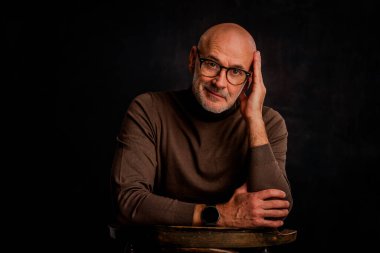 Siyah arka planda oturan balıkçı yaka kazaklı orta yaşlı bir adam. İzole edilmiş arka plan. Boşluğu kopyala.