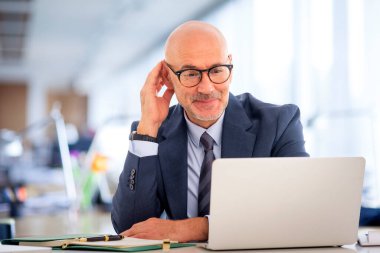 Ofisteki masasında dizüstü bilgisayarıyla çalışan orta yaşlı bir iş adamı. Profesyonel erkek, özenle dizüstü bilgisayara bakıyor..