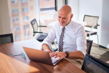 Orta yaşlı bir iş adamı masada oturup bilgisayar kullanıyor. Modern bir ofiste çalışan profesyonel bir erkek.. 