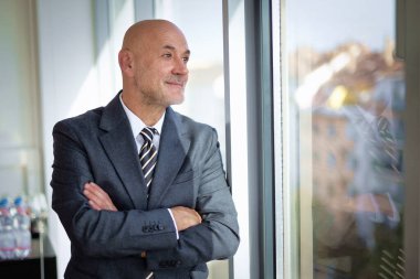 Ofiste duran orta yaşlı bir işadamı düşünceli bir şekilde bakıyor. Takım elbise giyen kendine güvenen profesyonel bir adam.. 