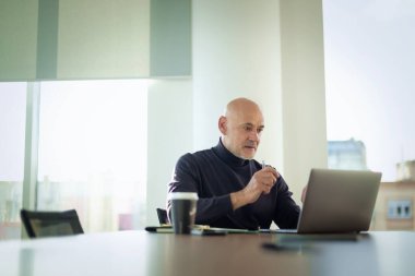 Orta yaşlı bir iş adamı modern bir ofiste dizüstü bilgisayarda çalışıyor. Gündelik kıyafetler giyen kendinden emin bir erkek.. 