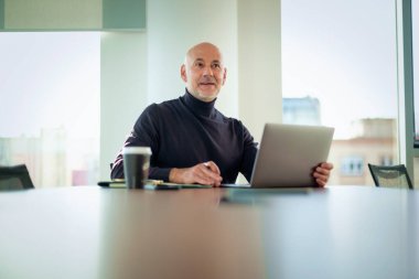 Orta yaşlı bir iş adamı modern bir ofiste dizüstü bilgisayarda çalışıyor. Gündelik kıyafetler giyen kendinden emin bir erkek.. 