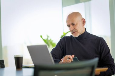 Orta yaşlı bir iş adamı modern bir ofiste dizüstü bilgisayarda çalışıyor. Gündelik kıyafetler giyen kendinden emin bir erkek.. 