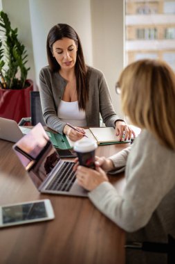 Modern bir ofiste masa başında oturan ve dizüstü bilgisayarlarla çalışan iki iş kadını. Takım çalışması. Bir grup iş adamı toplantı sırasında tartışıyor.