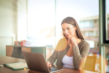 Ofis masasında çalışırken bilgisayarını kullanan çekici bir iş kadını. İş kıyafeti giyen profesyonel bir kadın.. 