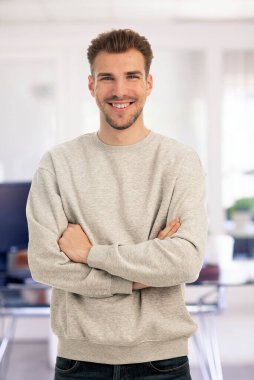 Modern bir ofiste tek başına dururken gülümseyen kendinden emin genç bir iş adamının portresi. Gündelik kıyafetler giyen genç girişimci. 
