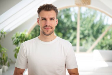 Kameraya bakıp gülümseyen genç bir adamın vesikalığı. Beyaz gömlekli ve kapalı bir yerde duran kendine güvenen bir adam.. 